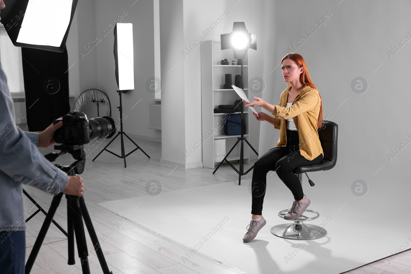 Photo of Casting call. Emotional woman with script performing while camera operator filming her against light grey background in studio