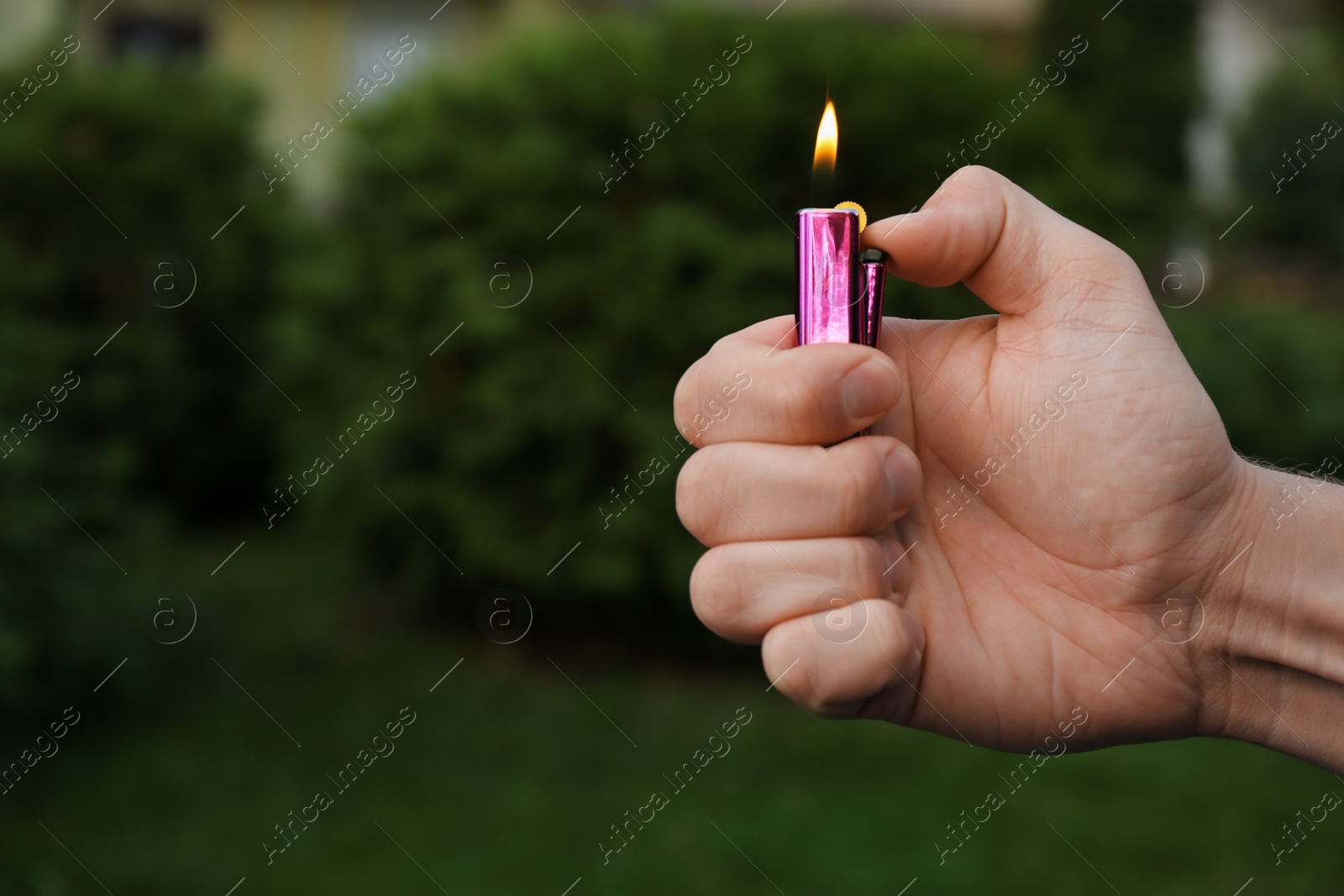 Photo of Man holding lighter with burning flame outdoors, closeup. Space for text