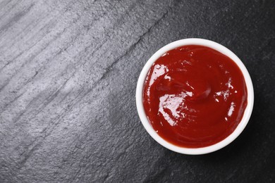 Photo of Organic ketchup in bowl on black table, top view with space for text. Tomato sauce