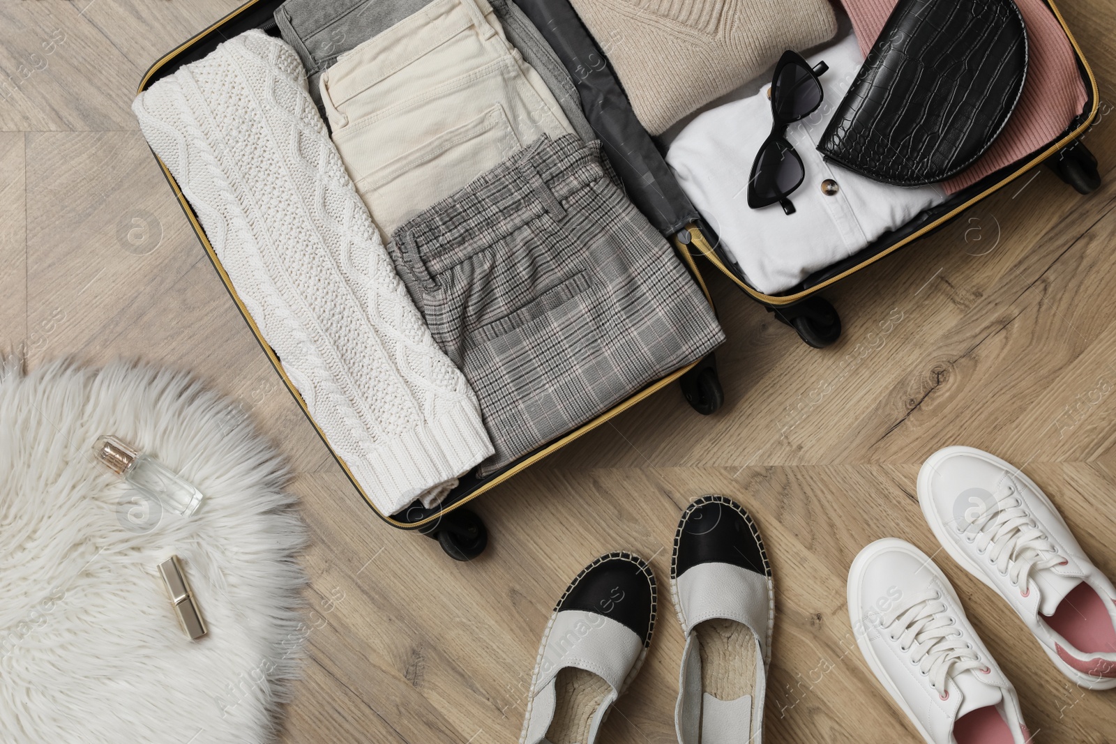 Photo of Open suitcase with folded clothes, accessories and shoes on floor, flat lay