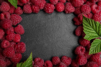 Photo of Frame of fresh ripe raspberries with green leaves on black table, flat lay. Space for text