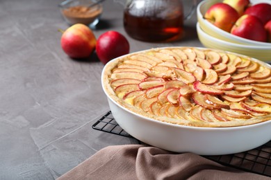Photo of Tasty apple pie in baking dish on grey table. Space for text
