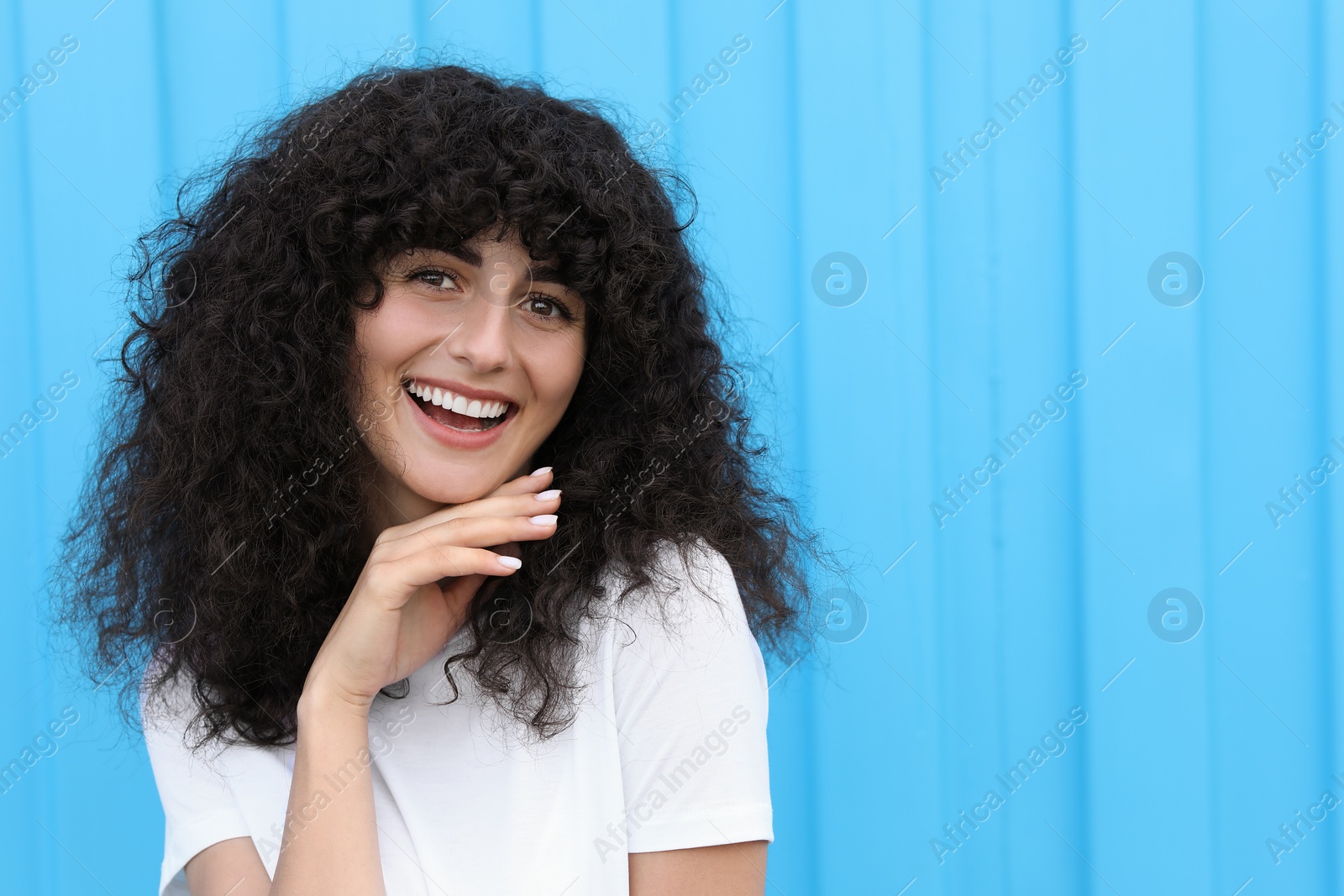 Photo of Portrait of beautiful woman posing near light blue wall. Attractive lady smiling and looking into camera. Space for text