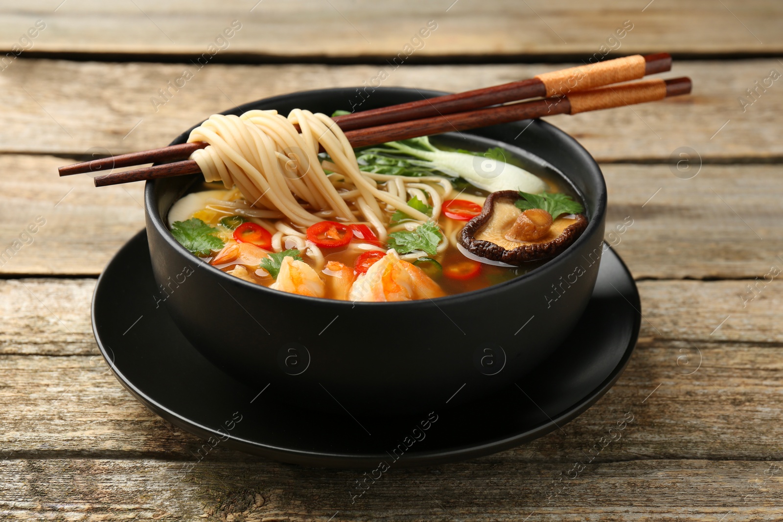 Photo of Bowl of delicious ramen with chopsticks on wooden table. Noodle soup