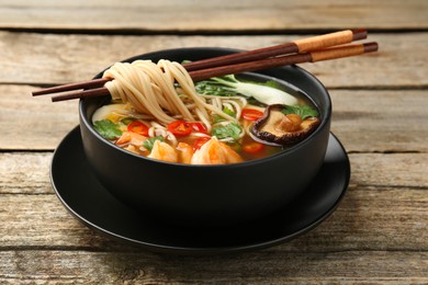 Photo of Bowl of delicious ramen with chopsticks on wooden table. Noodle soup