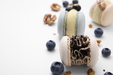 Photo of Delicious macarons, walnuts and blueberries on white table, closeup. Space for text