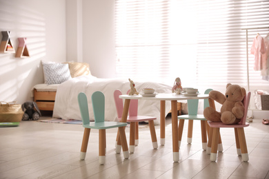 Photo of Small table and chairs with bunny ears in children's room interior