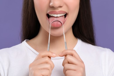 Photo of Woman brushing her tongue with cleaner on violet background, closeup
