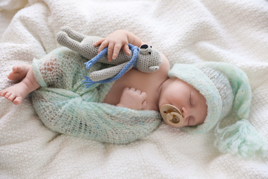 Cute newborn baby in warm hat with toy sleeping on white plaid, top view