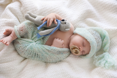 Photo of Cute newborn baby in warm hat with toy sleeping on white plaid, top view