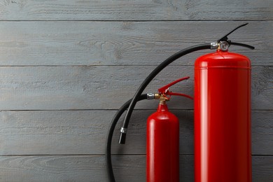Fire extinguishers on grey wooden background, flat lay. Space for text