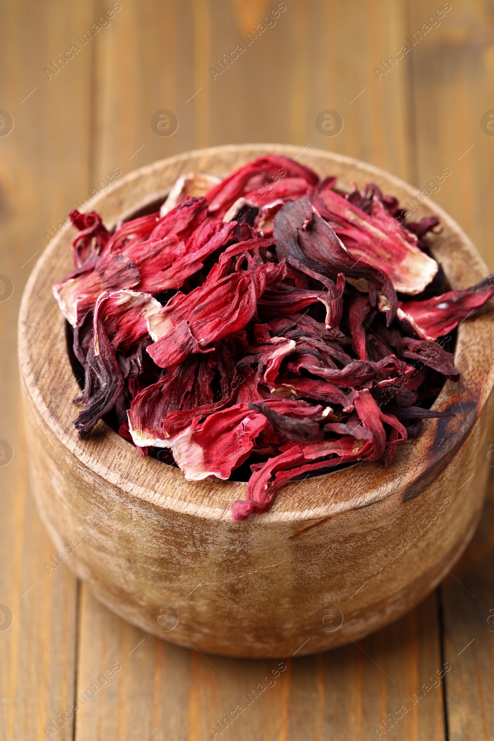 Photo of Dry hibiscus tea in bowl on wooden table, closeup
