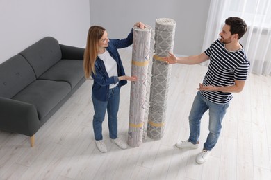 Photo of Smiling couple holding rolled carpets in room