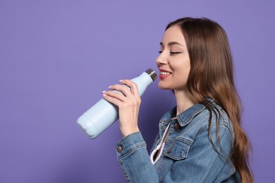 Photo of Beautiful young woman with thermos bottle on purple background