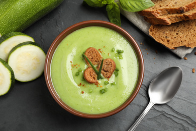 Photo of Tasty homemade zucchini cream soup served on black table, flat lay