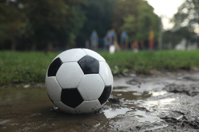 Dirty leather soccer ball in puddle outdoors