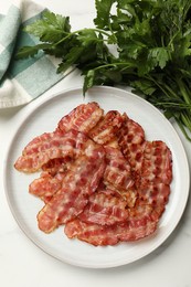 Plate with fried bacon slices and parsley on white table, top view