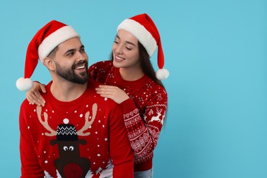 Photo of Happy young couple in Christmas sweaters and Santa hats on light blue background. Space for text