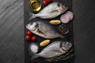 Photo of Fresh raw dorado fish, lemon wedges, spices and tomatoes on black table, flat lay