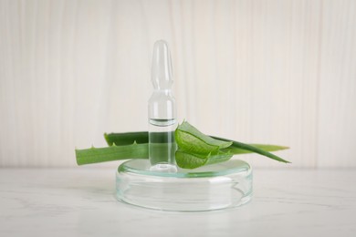 Photo of Pharmaceutical ampoule with medication and aloe leaves on white table