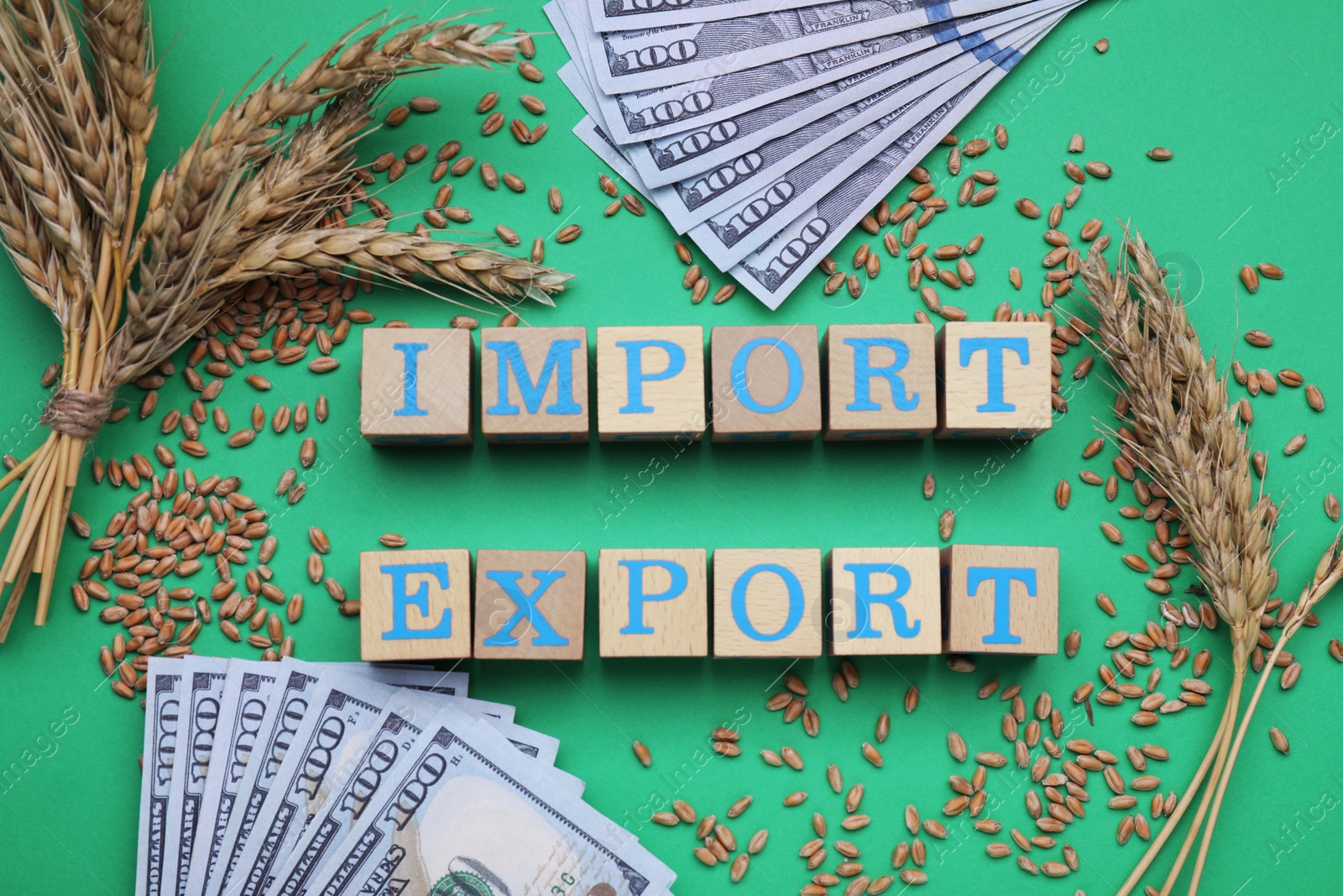 Photo of Words Import and Export made of wooden cubes, ears of wheat and banknotes on green background, flat lay