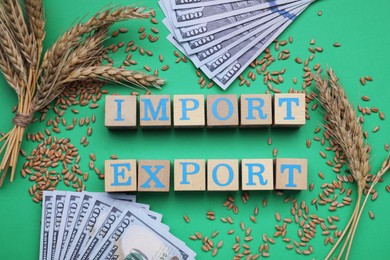 Photo of Words Import and Export made of wooden cubes, ears of wheat and banknotes on green background, flat lay