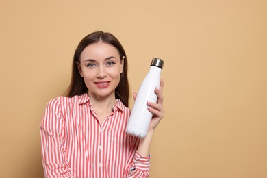 Photo of Beautiful young woman with thermos bottle on beige background, space for text