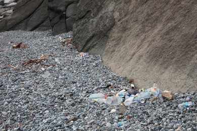 Photo of Garbage scattered on pebbles near rock. Recycling problem