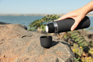 Photo of Woman pouring hot drink from thermos into cap outdoors, closeup