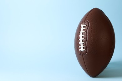 Photo of American football ball on light blue background. Space for text