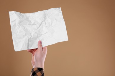 Photo of Man holding sheet of crumpled paper on pale orange background, closeup. Mockup for design