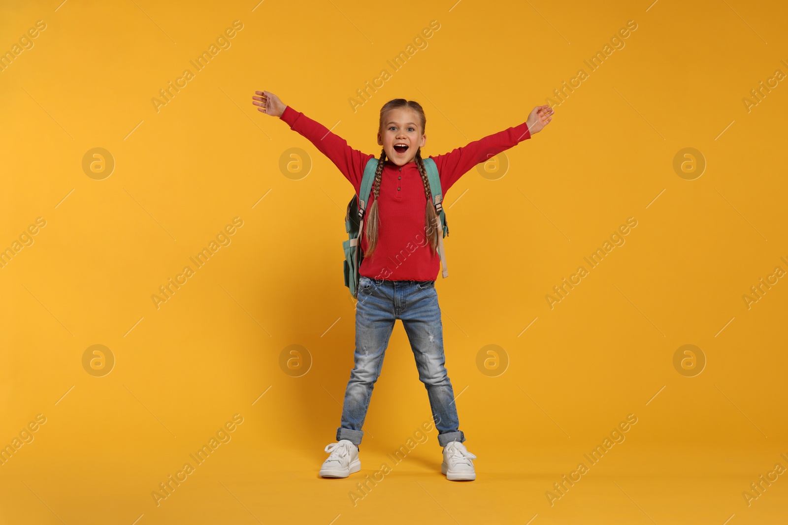 Photo of Emotional schoolgirl with backpack on orange background