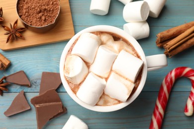 Photo of Tasty hot chocolate with marshmallows and ingredients on light blue wooden table, flat lay