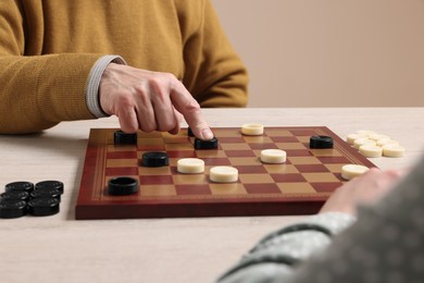 Photo of Senior man playing checkers with partner at white wooden table, closeup