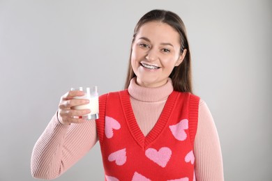 Photo of Happy woman with milk mustache holding glass of drink on light grey background