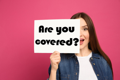 Image of Woman holding paper with text ARE YOU COVERED? on pink background. Insurance concept