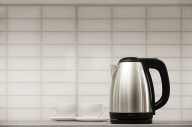 Photo of Modern electric kettle and cups on grey kitchen counter. Space for text