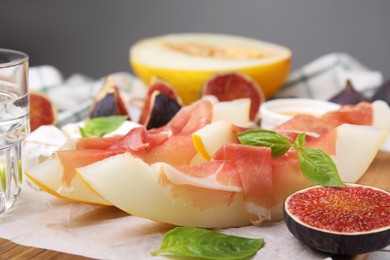Photo of Tasty melon, jamon and figs served on wooden board