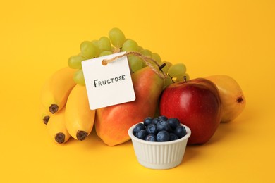 Photo of Card with word Fructose, delicious ripe fruits and blueberries on yellow background
