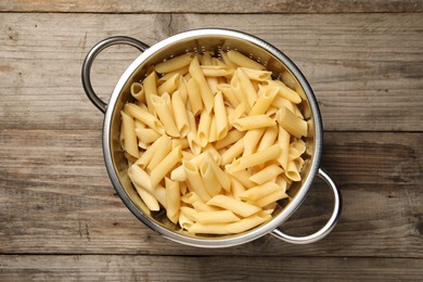 Photo of Delicious penne pasta in colander on wooden table, top view