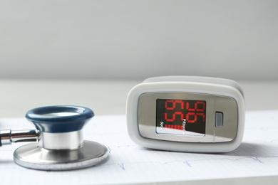 Photo of Modern fingertip pulse oximeter, stethoscope and cardiogram on grey table, closeup