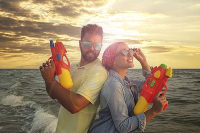 Photo of Happy couple with water guns near sea at sunset