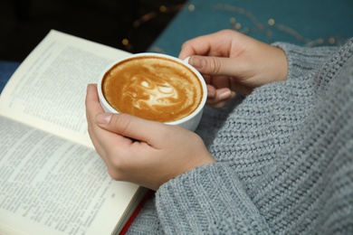 Photo of Woman with cup of coffee reading book at home, closeup