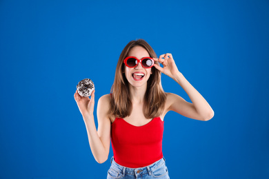 Photo of Beautiful young woman wearing sunglasses with donut on blue background