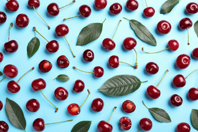 Photo of Sweet juicy cherries with leaves on light blue background, flat lay