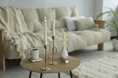 Photo of Burning candles, vase, cup of hot drink and wristwatch on wooden table in living room. Space for text