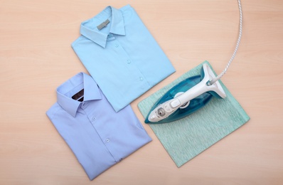 Photo of Folded clean clothes and iron on wooden background, top view