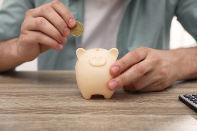 Photo of Man putting coin into piggy bank at wooden table, closeup