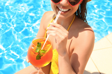 Photo of Woman with glass of refreshing drink near swimming pool, closeup