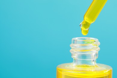 Photo of Dripping yellow serum from pipette into bottle on light blue background, closeup. Space for text